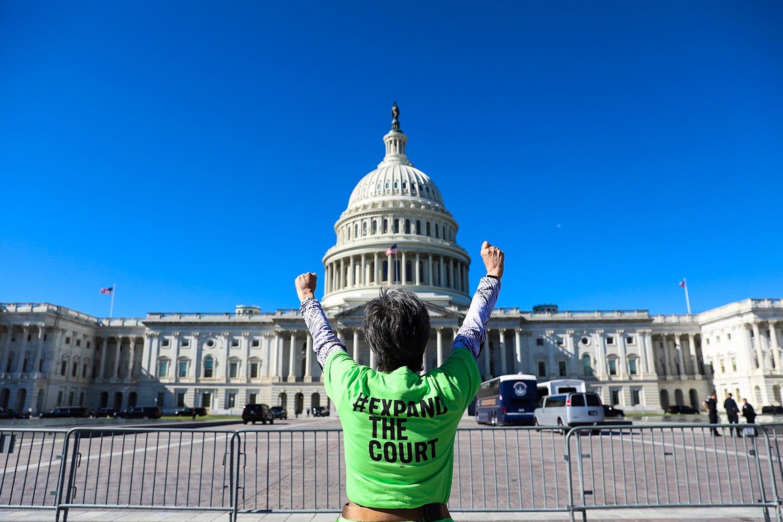 woman standing in front of the capitol building with her hands in the air and her back to the camera, wearing a green shirt that says expand the court
