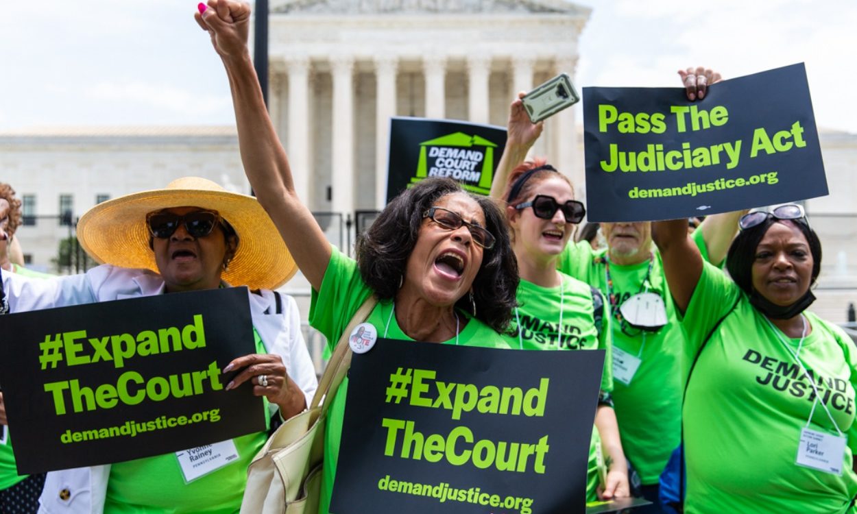 image of demand justice volunteers standing outside the supreme court, wearing bright green t-shirts, and holding signs that say expand the court