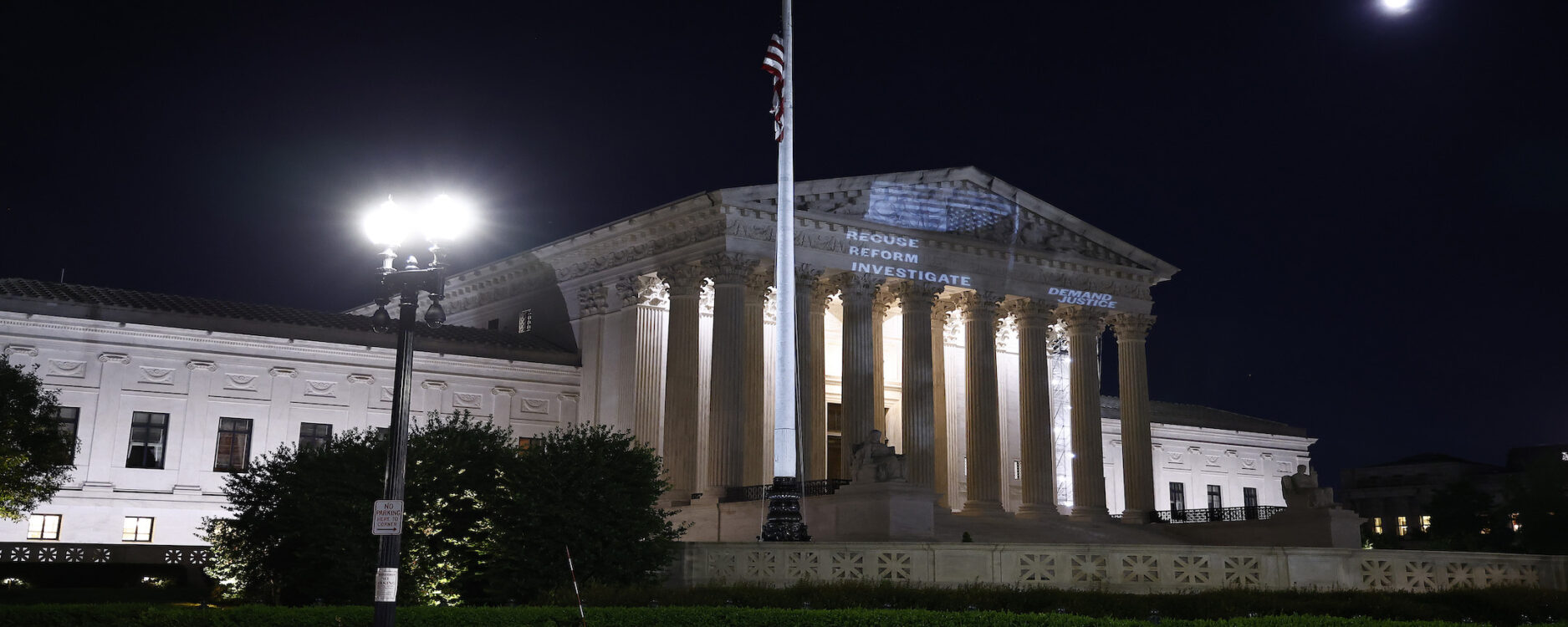 A photo of the Supreme Court with the words "recuse, reform, investigate" and an upside down American flag projected onto it.